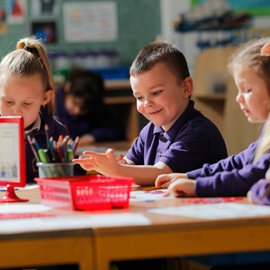 Children engaged in activities at a classroom table, with art supplies and colourful papers scattered around them.