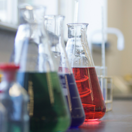 Three glass conical flask on a counter, each contains different coloured liquids, one red, one blue and one green for use in science lessons.