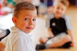 Young primary aged boy wearing a white polo smiles at the camera  engaged in an activity.