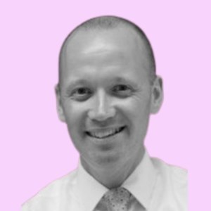 Smiling person in a formal shirt and tie, set against a light pink background. The image is grayscale