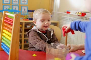 ALT child sitting at desk holding a stacker with another child, with an abacus next to him