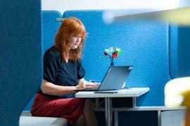 Woman with red hair working on a laptop in a blue, cosy office booth.