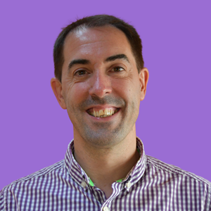 Smiling man in a checkered shirt, set against a purple background. 