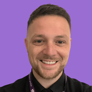 A smiling person with short hair, wearing a dark shirt and lanyard, against a solid purple background.