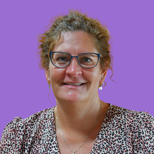 A woman with glasses smiles against a purple background. She has curly hair and wears a leopard print top