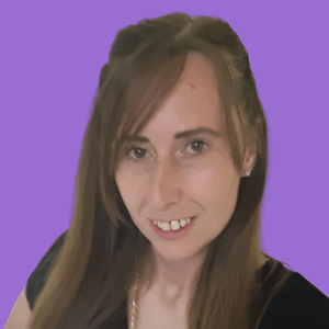 A woman with long brown hair and a warm smile is in front of a solid purple background. She wears a black top