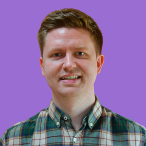 A smiling man with short brown hair wearing a green plaid shirt stands against a solid purple background
