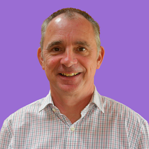 Smiling man with short hair in a checkered shirt, standing against a solid purple background.
