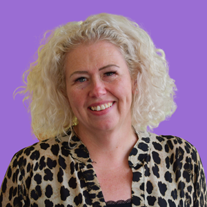 Smiling woman with curly blonde hair wearing a leopard print blouse, set against a purple background.