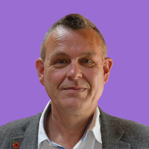 Portrait of a man with short hair wearing a grey blazer and white shirt, set against a purple background. 