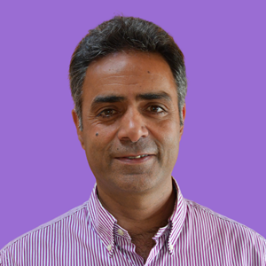 Smiling man in a striped pink shirt against a purple background. He has short dark hair and a relaxed expression