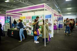 View of exhibition hall with various stands of exhibitors and people milling around the arena, speaking to exhibitors or looking at their stands