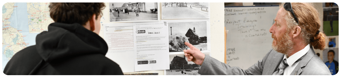 Older male pointing at a whiteboard showing a young male