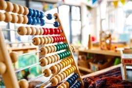 ALT Close-up of a colorful wooden abacus in a bright, sunlit classroom. Blue, red, green, and yellow beads stand out, evoking a playful and educational tone.