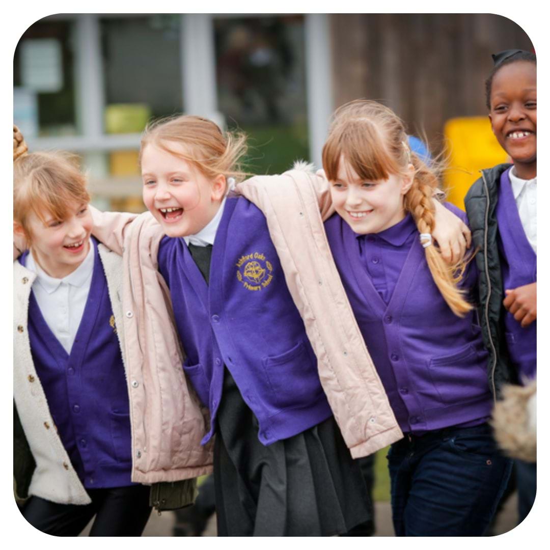 Four children in purple school uniforms walk arm in arm, smiling and laughing together. They appear joyful and are outside by a school building.