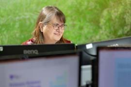 Lady sitting behind a computer, looking at the screen and smiling 