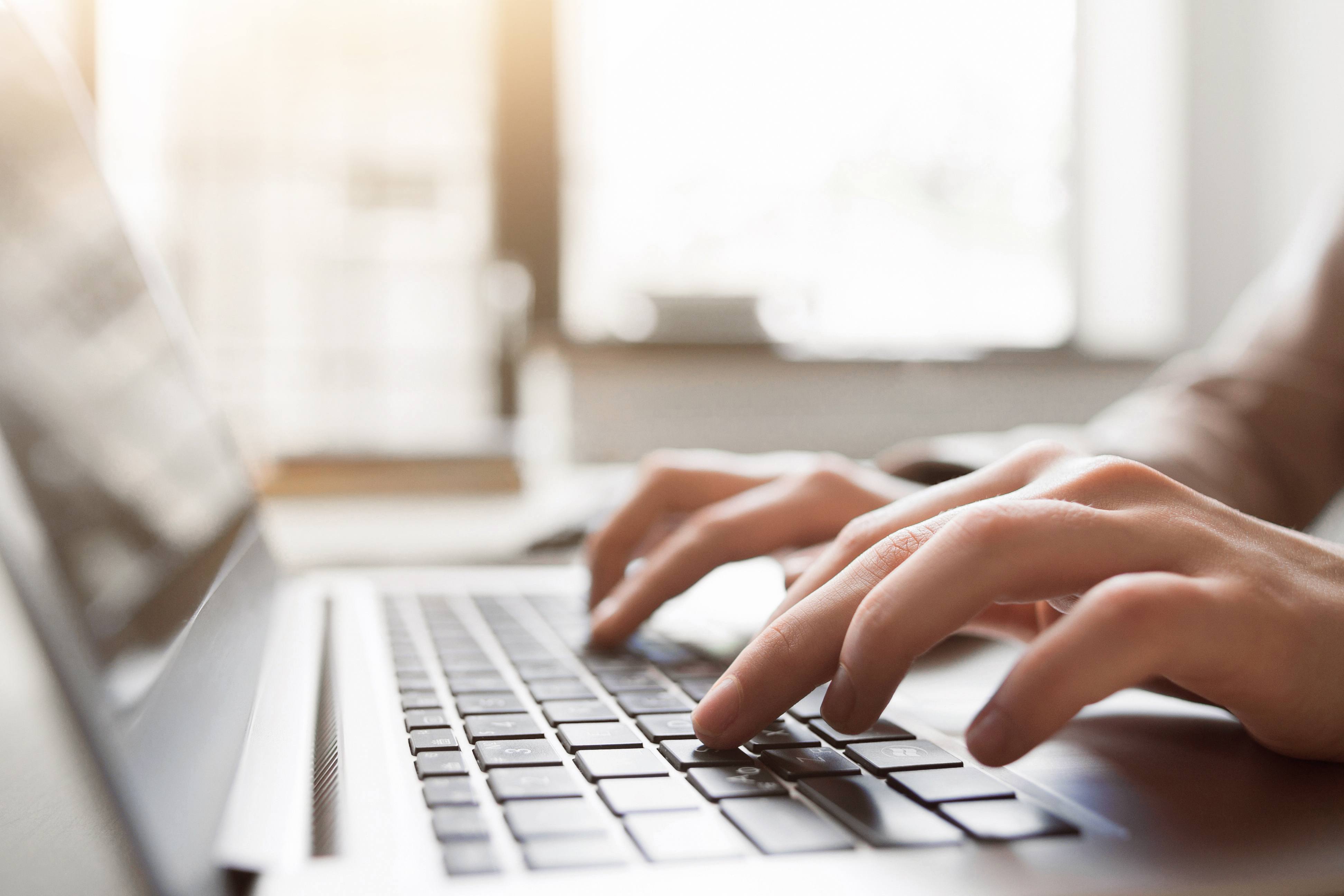 Person typing on a laptop, image shows their hands and the laptop with a blurred background