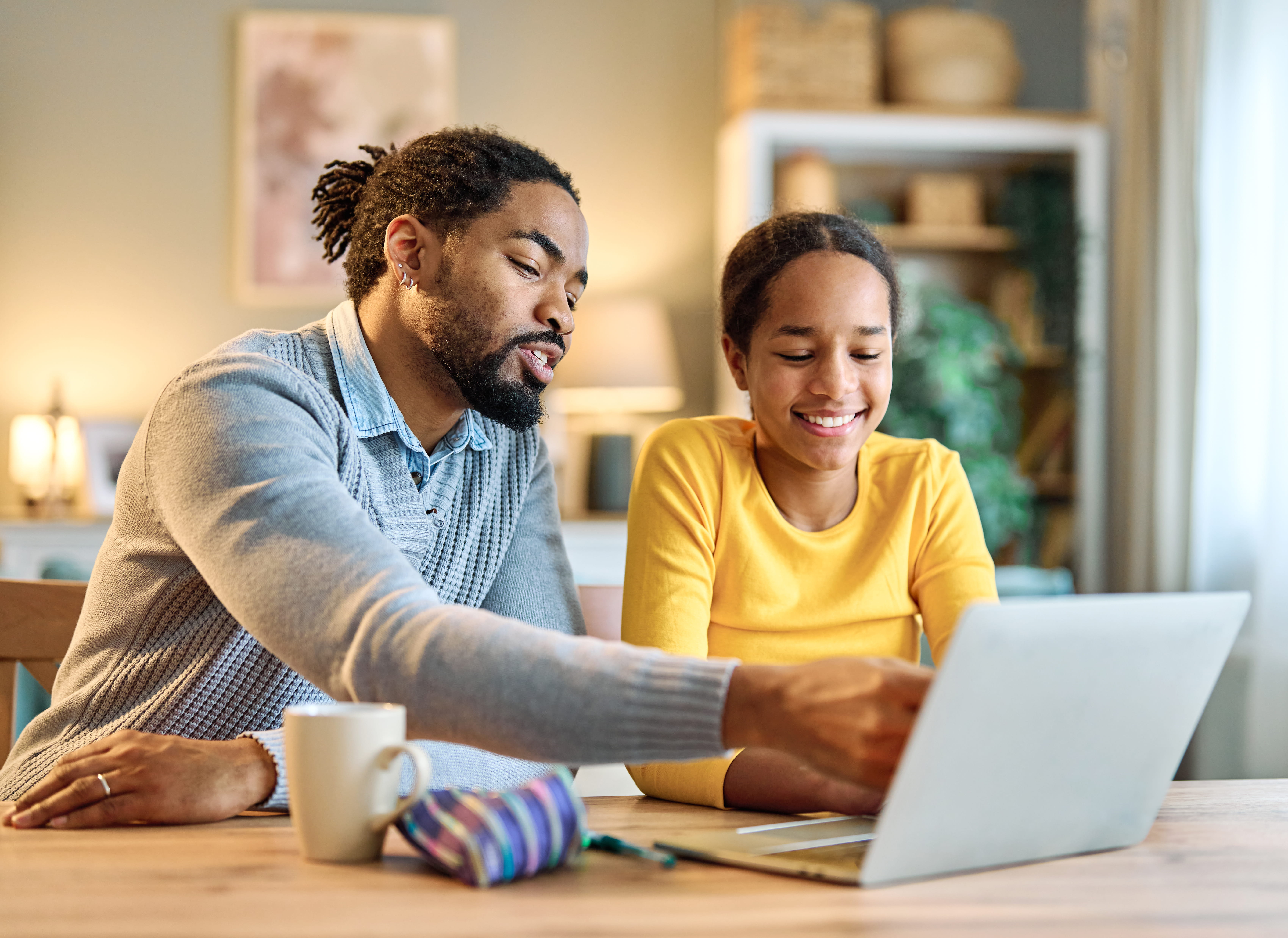 ALT - A man and young girl sit at a table, smiling and looking at a laptop.