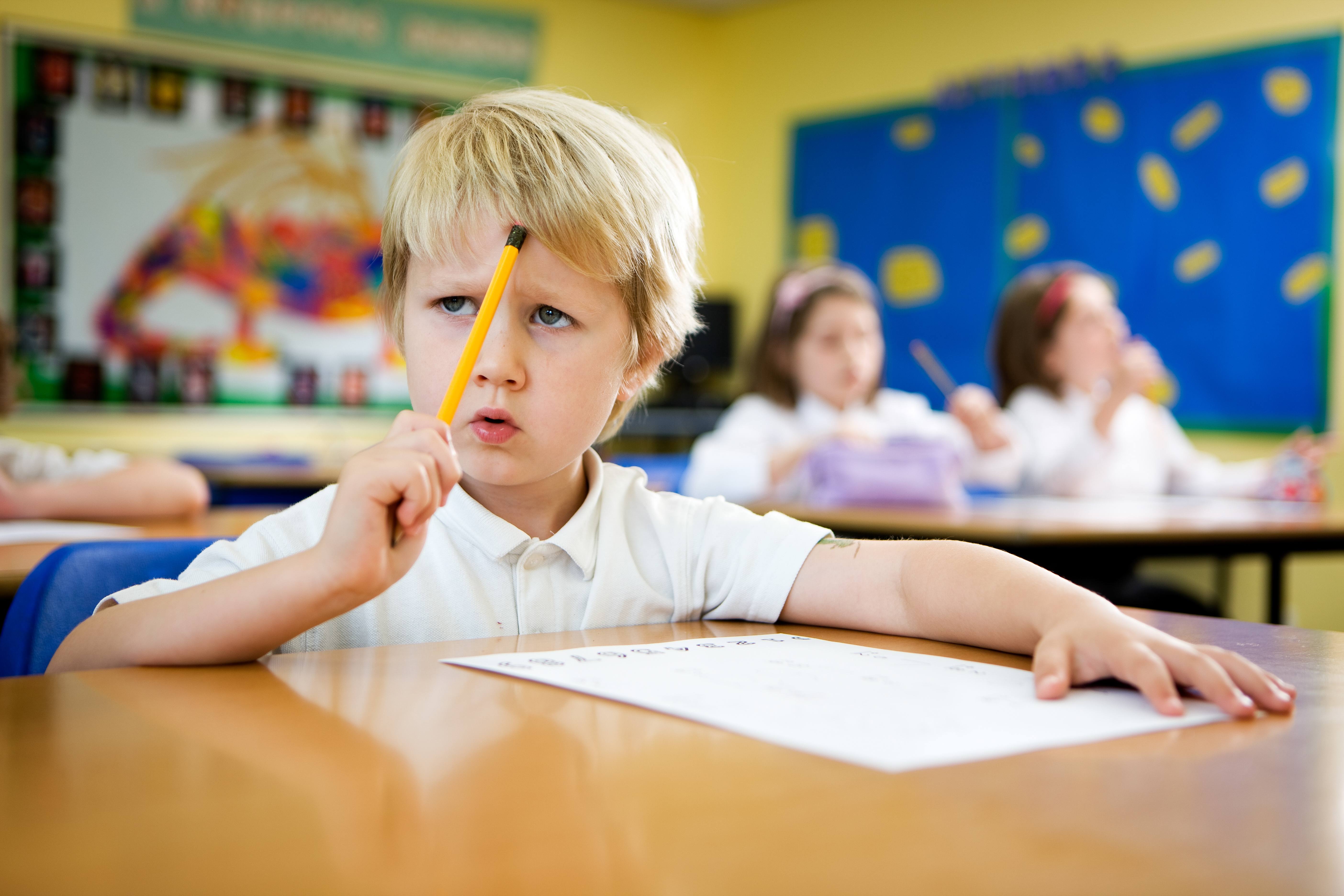 ALT - child sitting at desk with pencil in his hand holding it against his head with a concerned expression