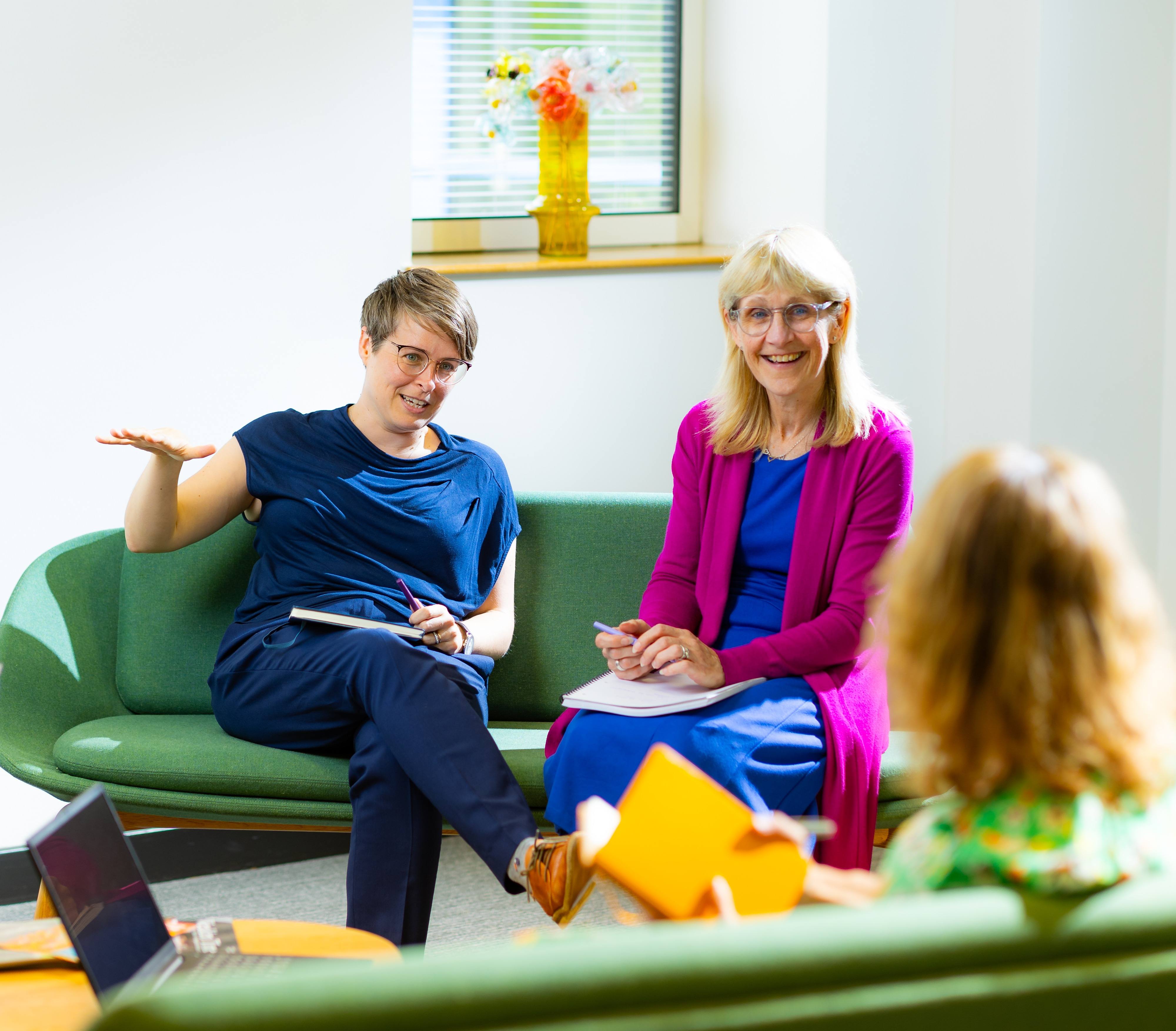 ALT - three ladies sitting on chairs having a conversation with notepads on their laps