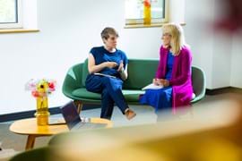 ALT - two ladies sitting on sofa having a conversation using their hands to express themselves