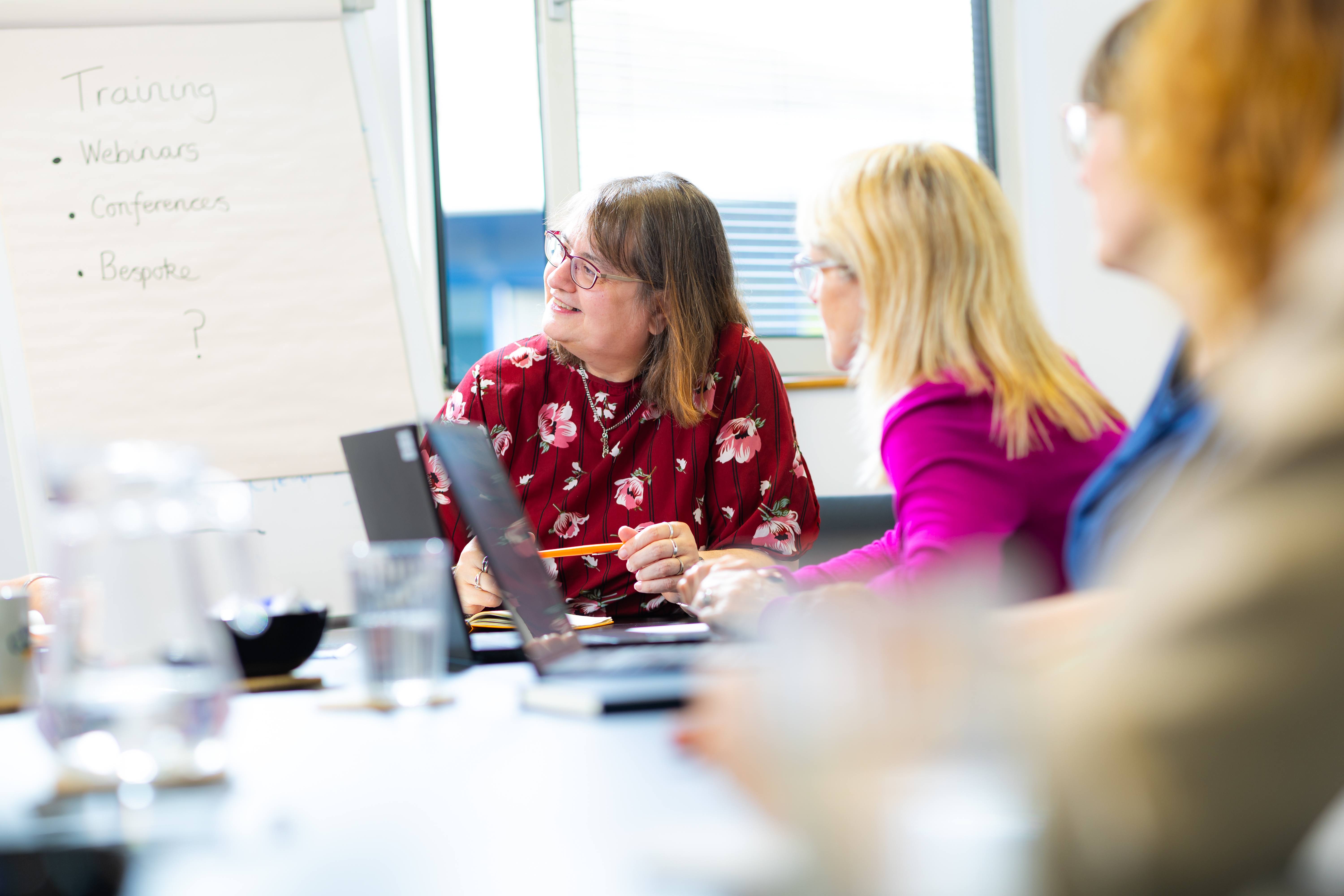 ALT - Ladies sitting around a desk having a conversation using laptops