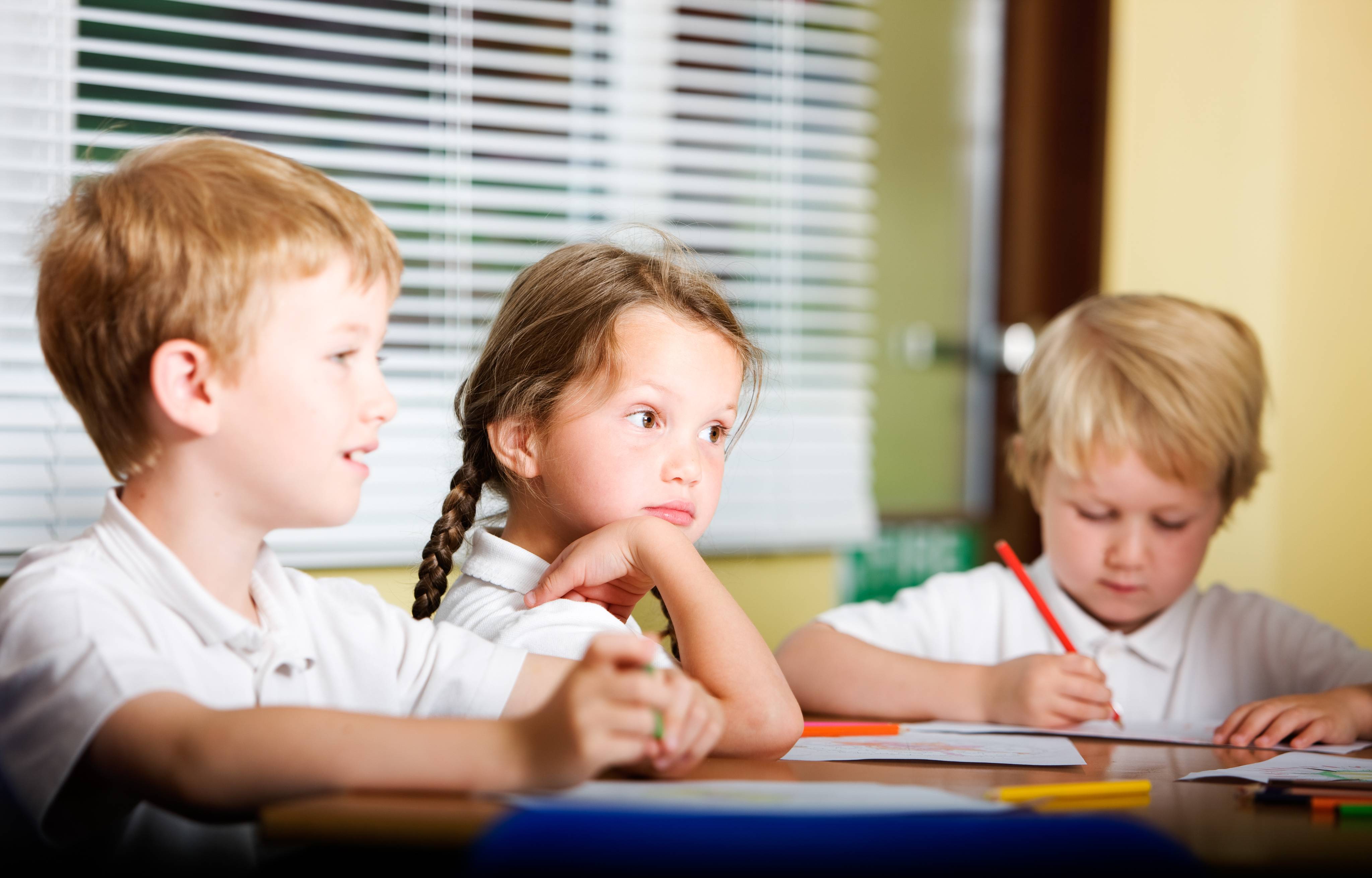 ALT - Children sitting around desk writing and listening