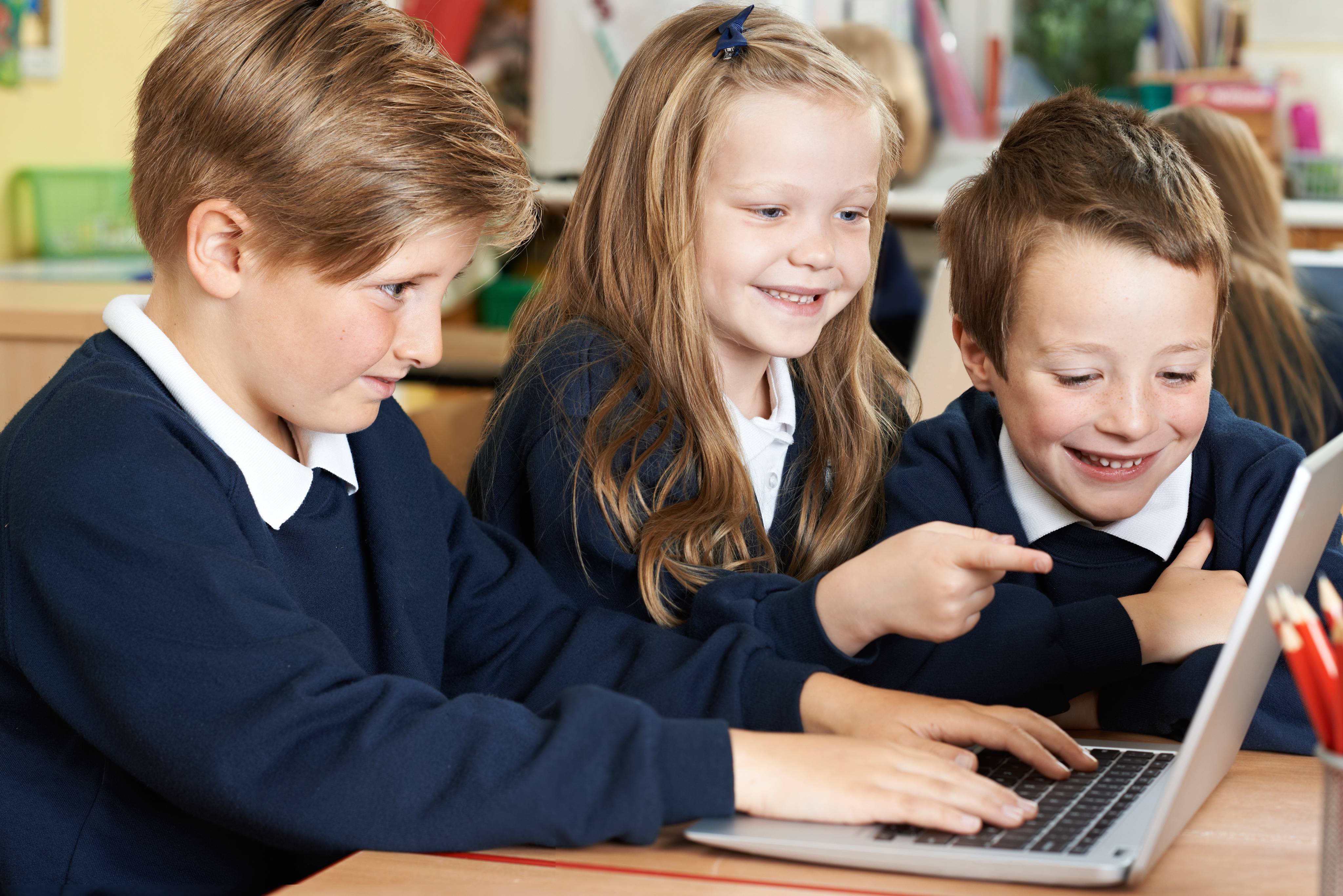 ALT - Three children sitting at a desk in front of a laptop smiling and laughing