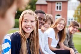 ALT - Teenage children sitting in a row smiling and talking to each other 