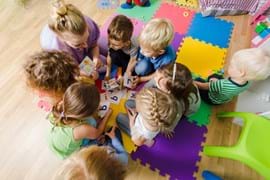 ALT - children sitting on the floor with a teacher looking at phonics cards