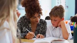 Alt - Teacher and child sitting at desk looking at an exercise book.