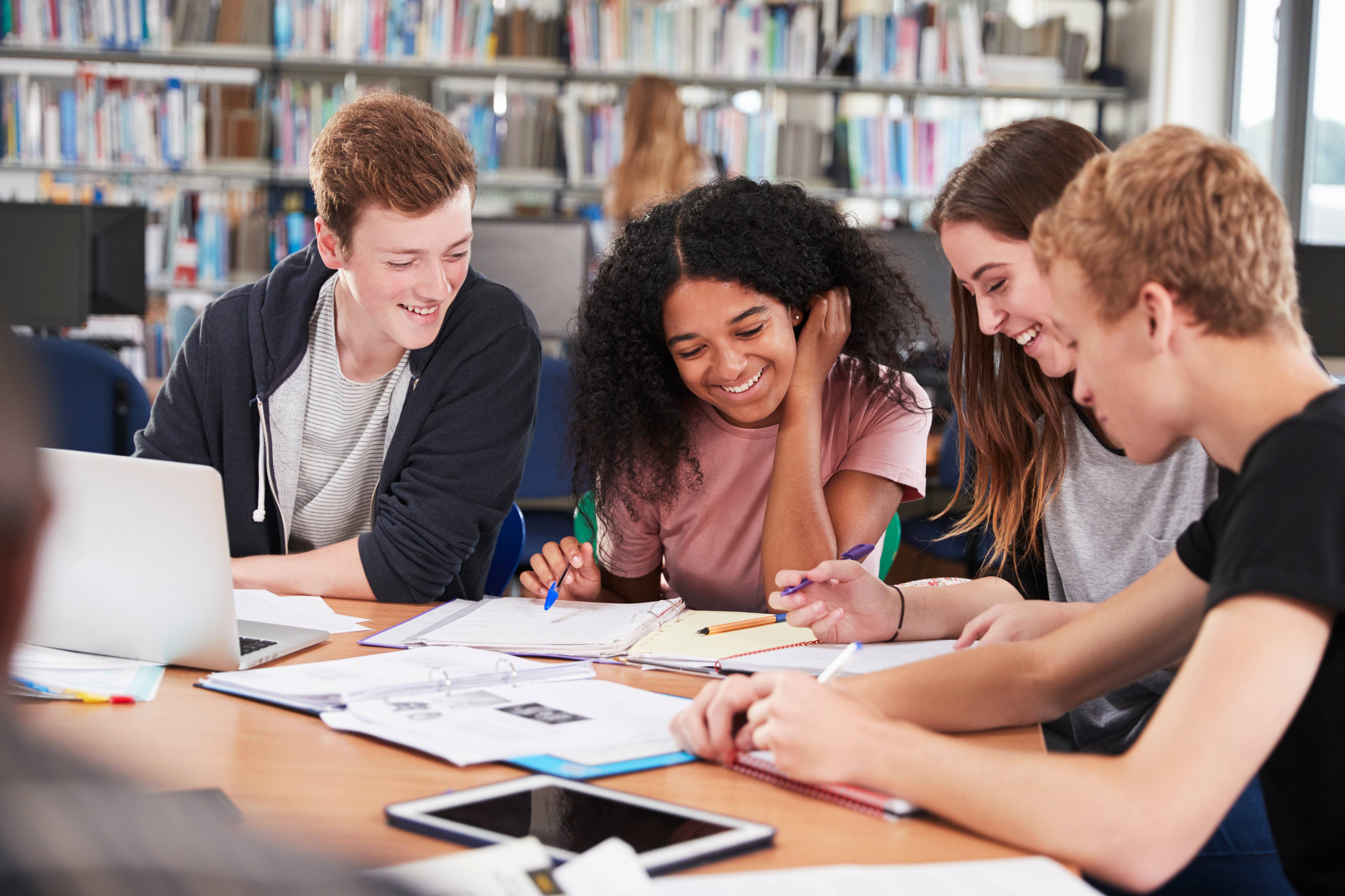 Alt - Teenagers sitting at a desk working and talking to each other