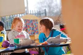 ALT - Nursery teacher and child sitting at a desk playing with toy sharks and drawing 
