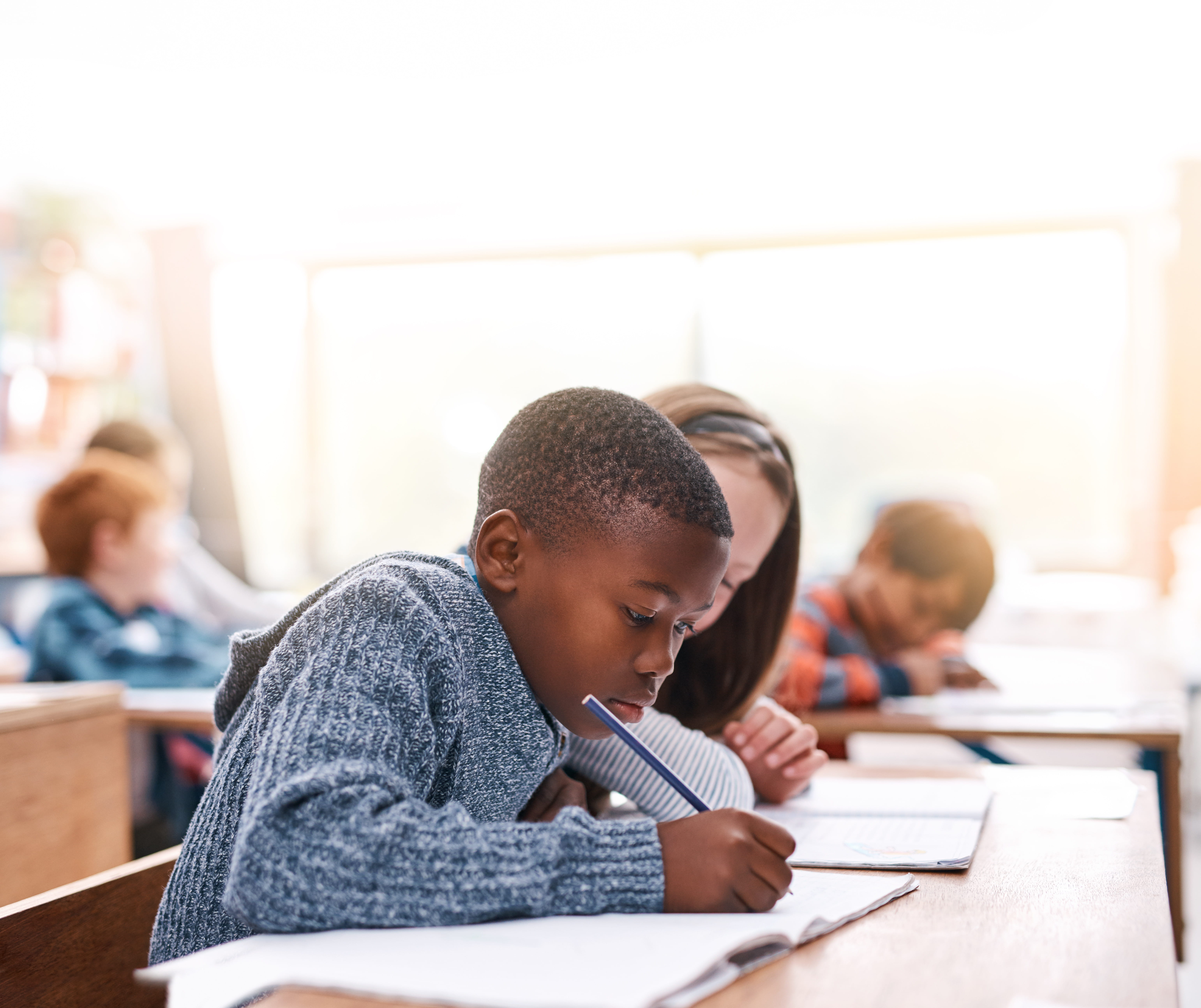 ALT - children sitting at desk writing in books