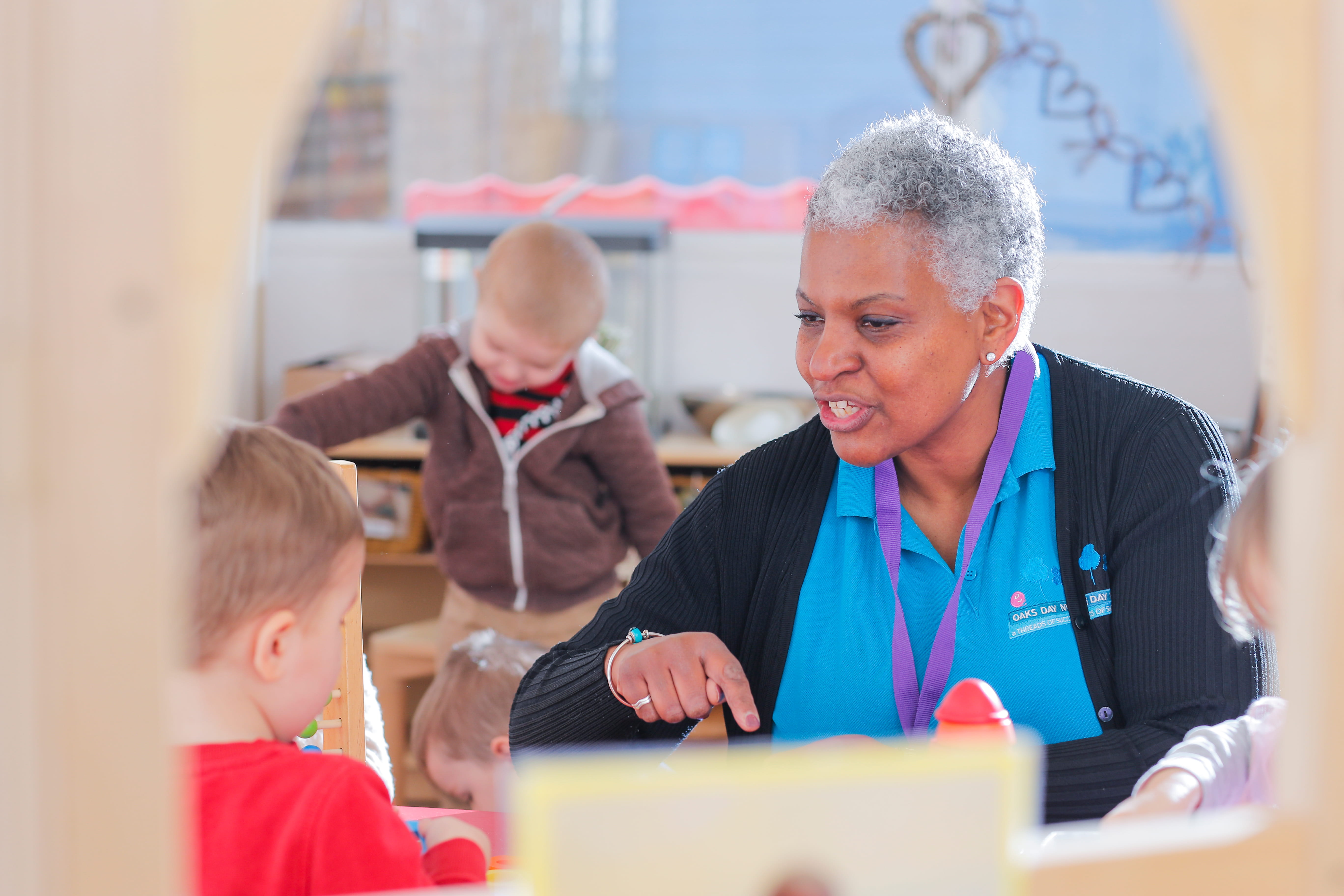 ALT - Nursery teacher sitting at a desk talking to a child