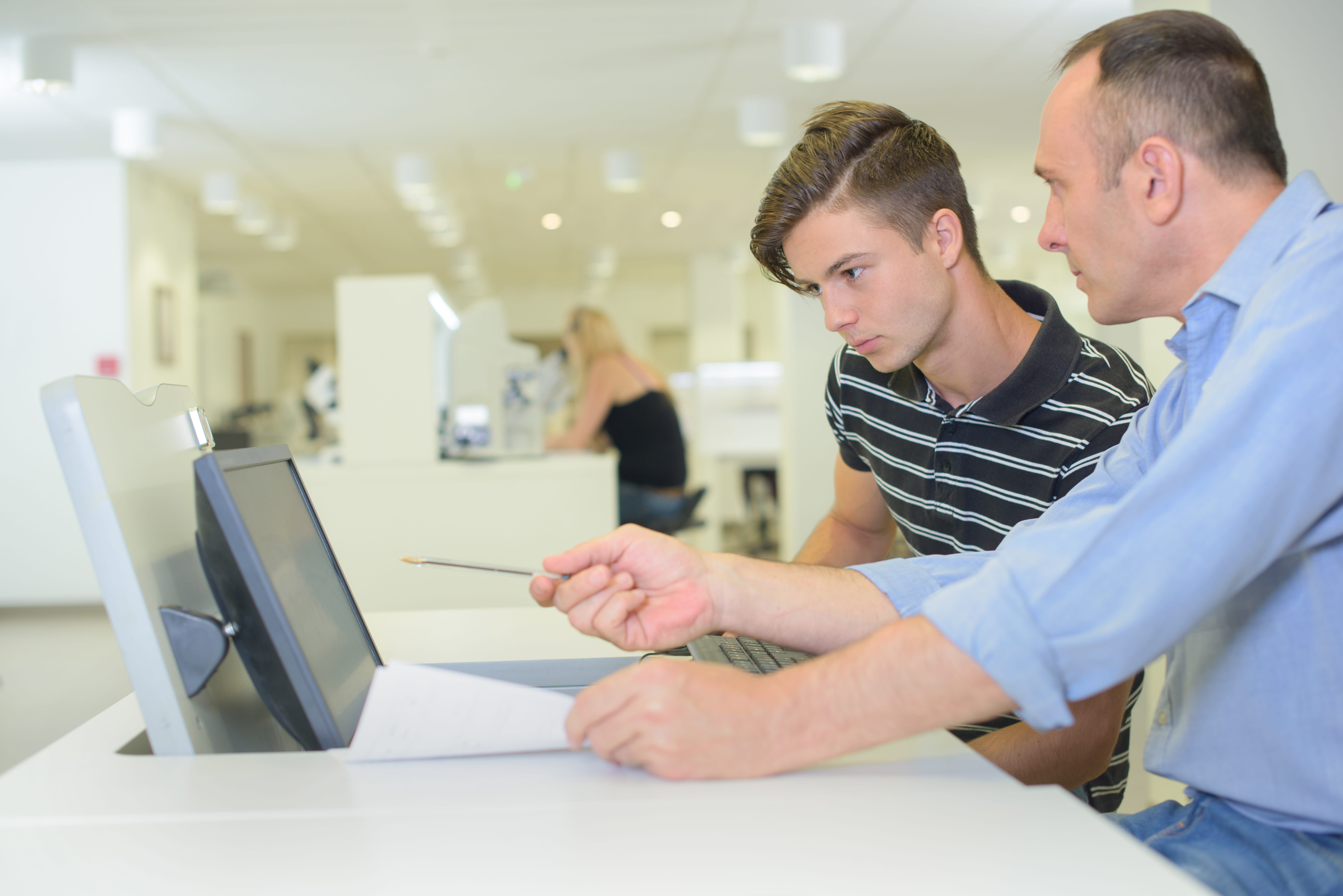 ALT - Teacher and teenage boy sitting in front of a computer having a conversation