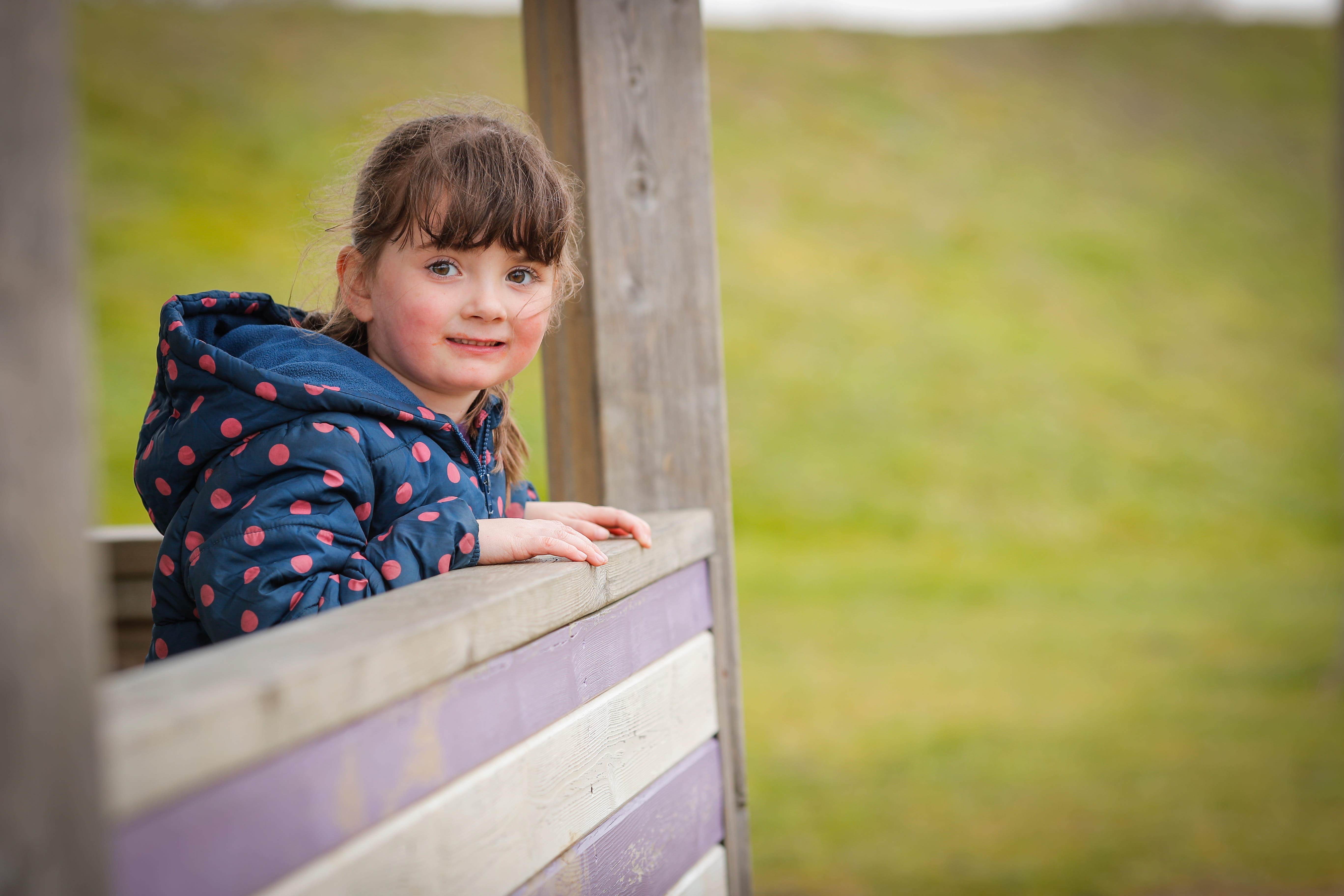 ALT - Child standing outside with her coat on leaning against a fence
