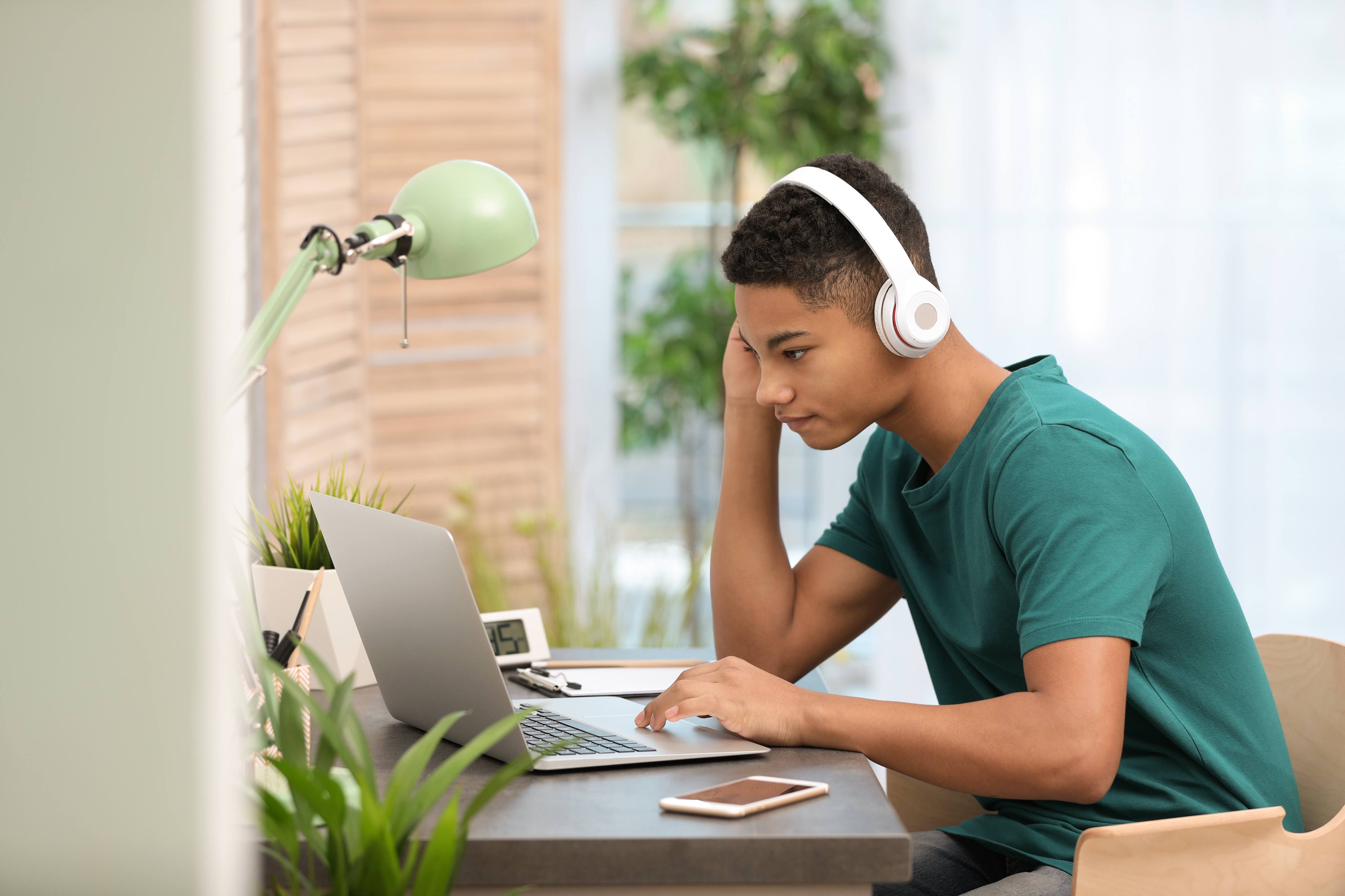 Young adult sitting at desk with headphones on using a laptop. 