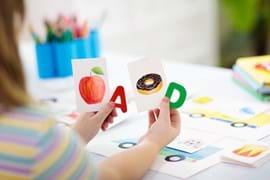 ALT - Child sitting at table holding the letter A with a picture for apple and D with a picture for donut in her hand