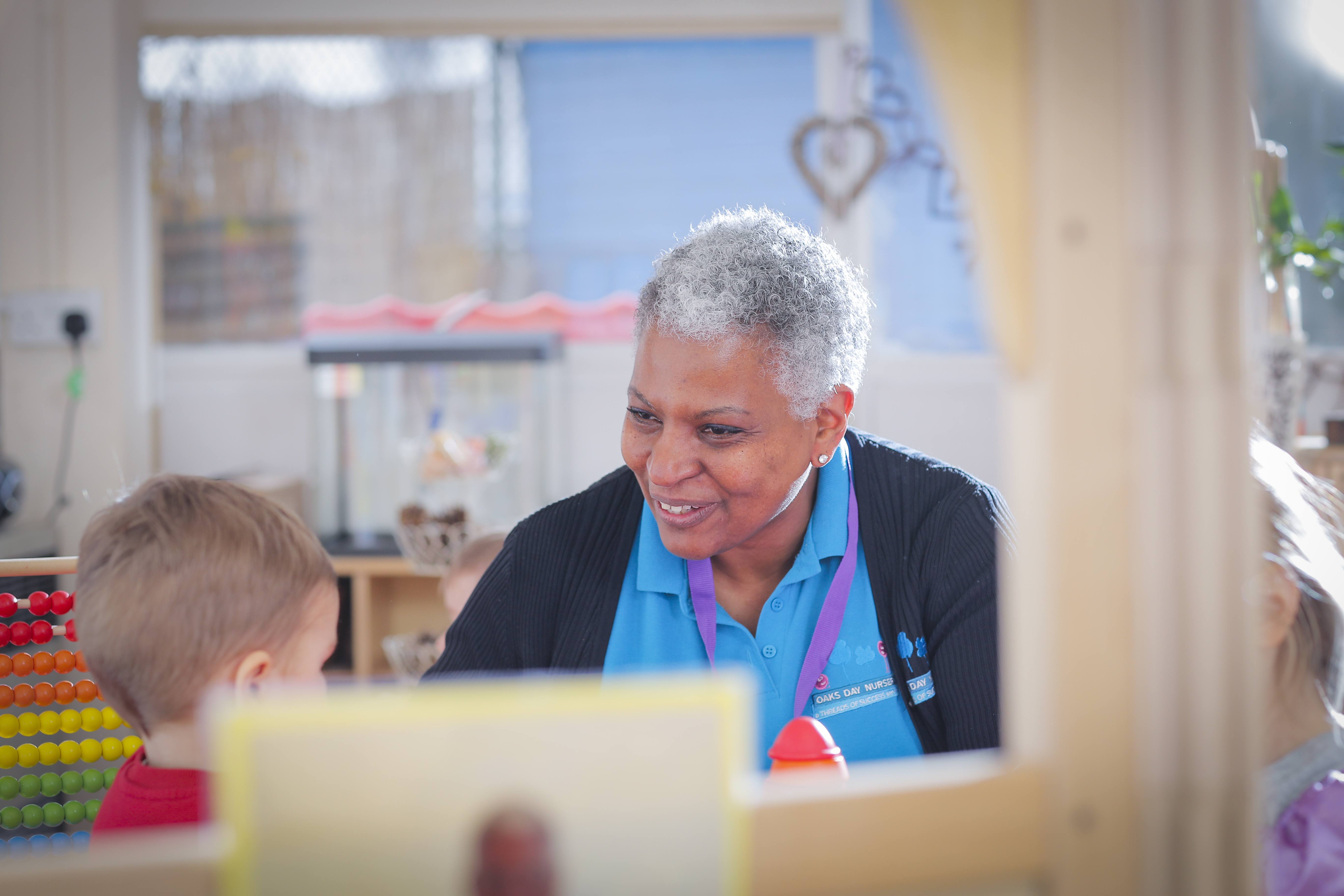 ALT - Nursery teacher sitting at a table talking to a child