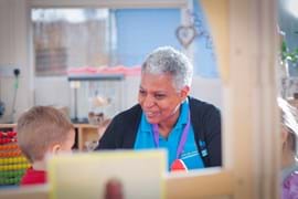 ALT - Nursery teacher sitting at a table talking to a child