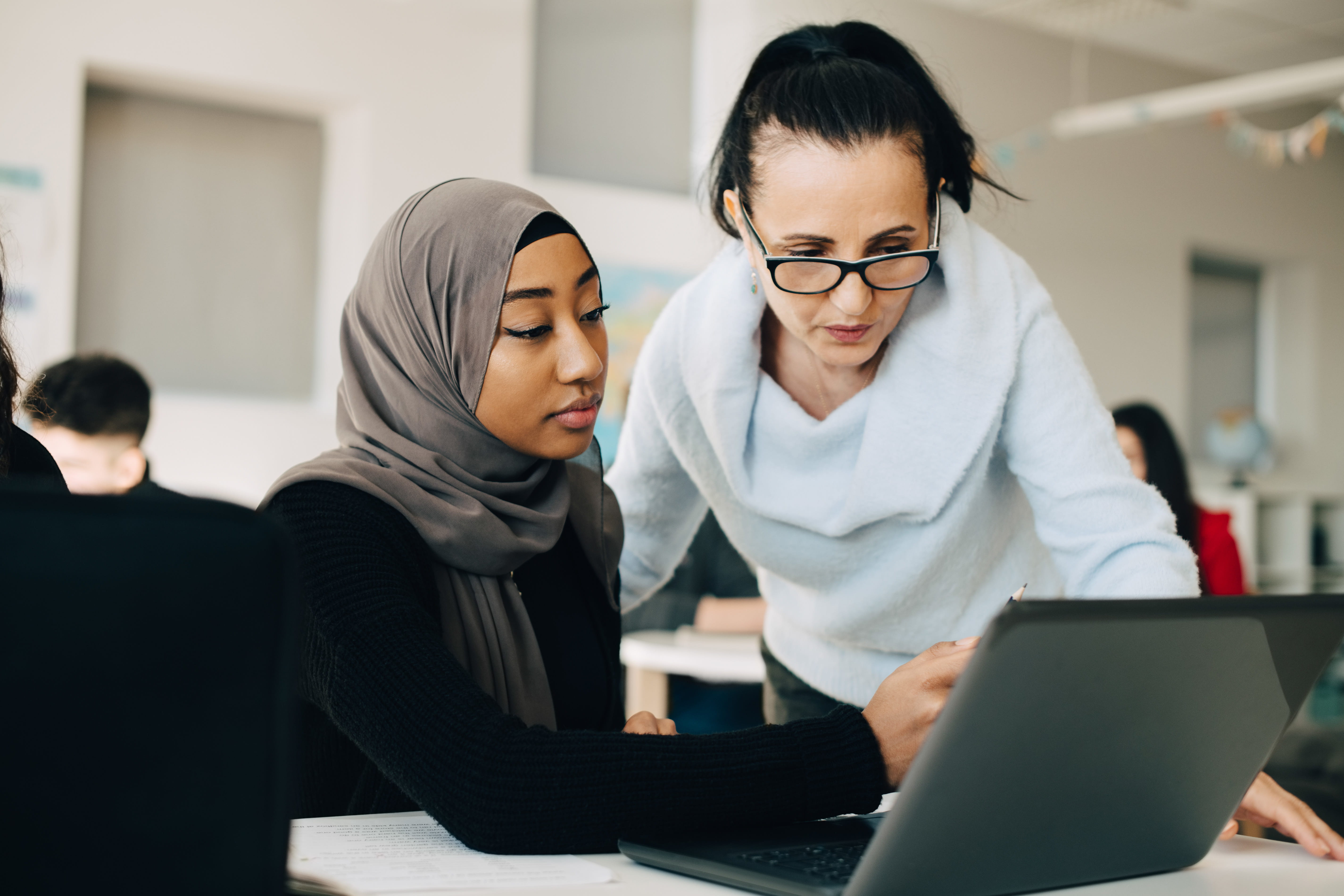 ALT - Lady sitting at a laptop, other lady standing looking at the screen having a conversation