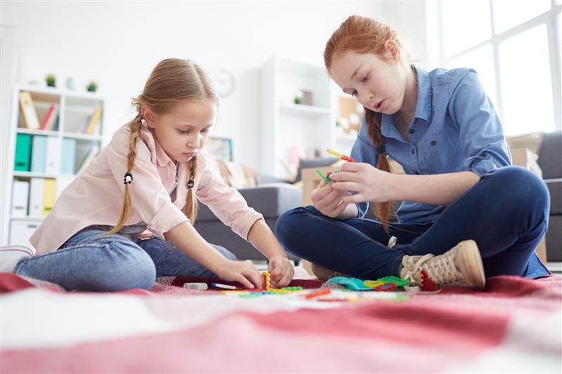 ALT - Two children sitting on the floor building making bracelets