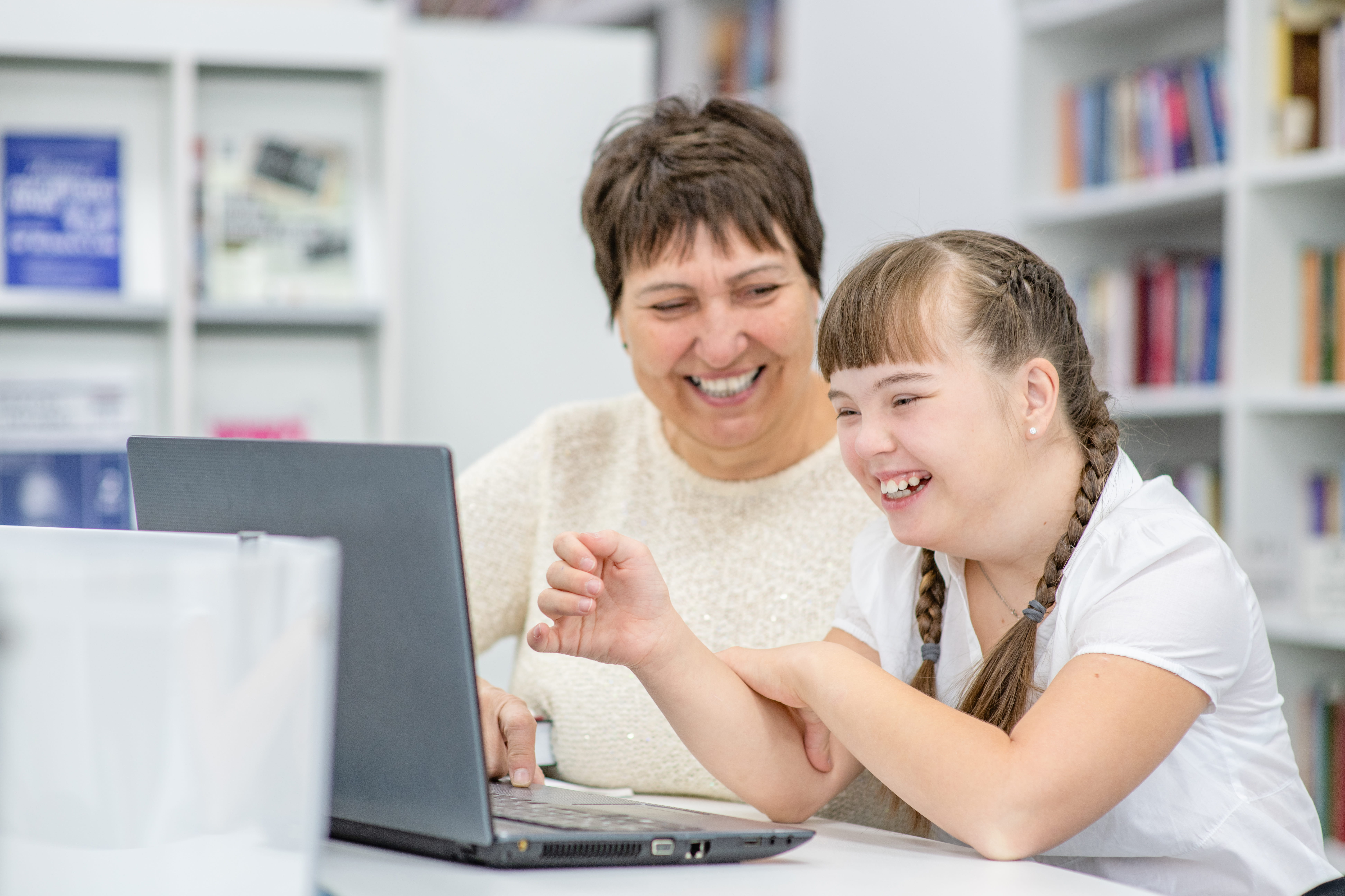 ALT - Teacher and child with special needs using a laptop, smiling and laughing
