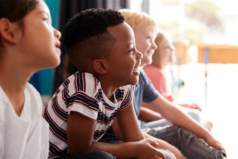 Four children sitting in a row, looking forward and laughing 