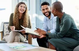 Three people are seated and engaged in a lively discussion in a bright office.