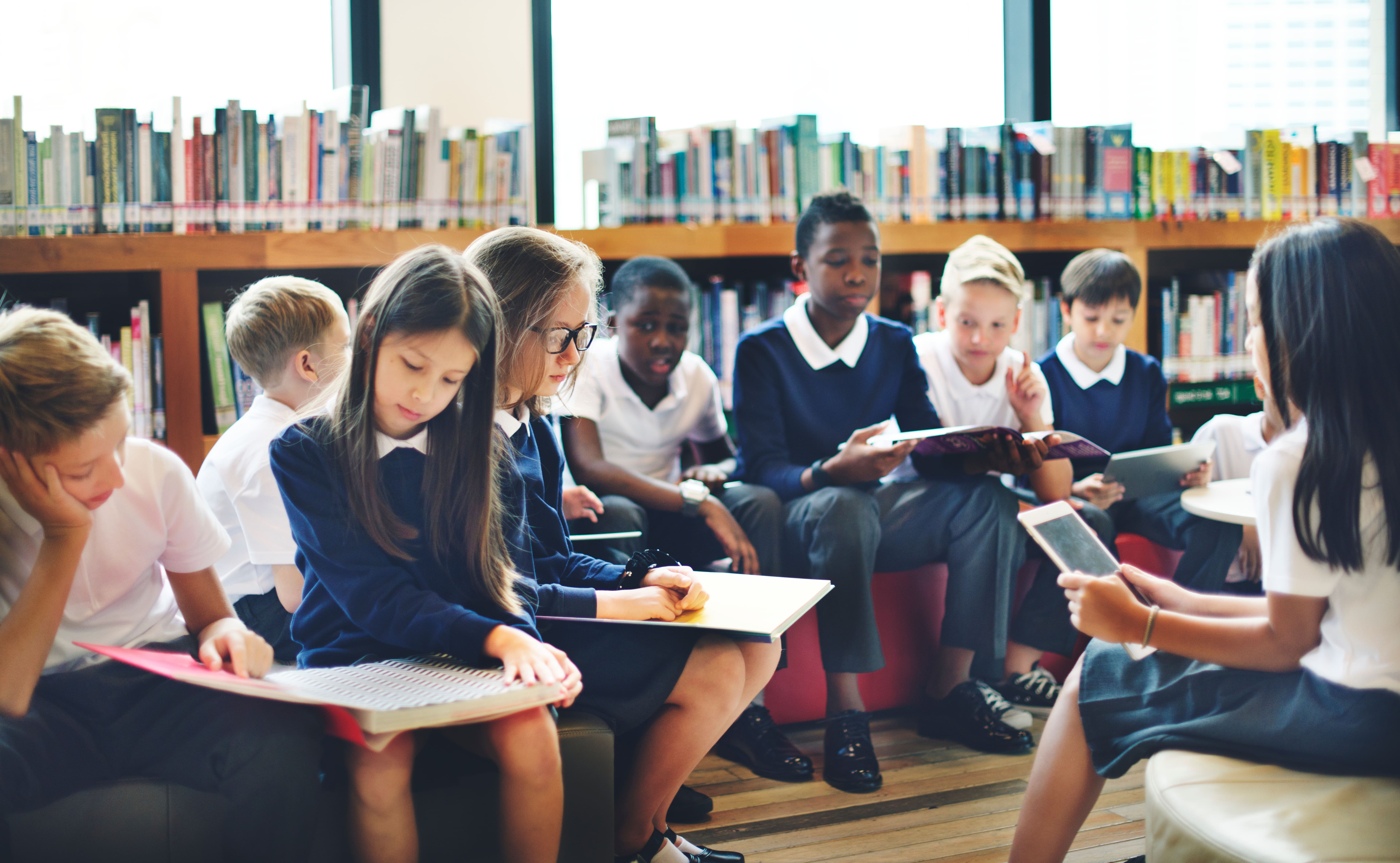A diverse group of children sits in a library, reading and discussing books.