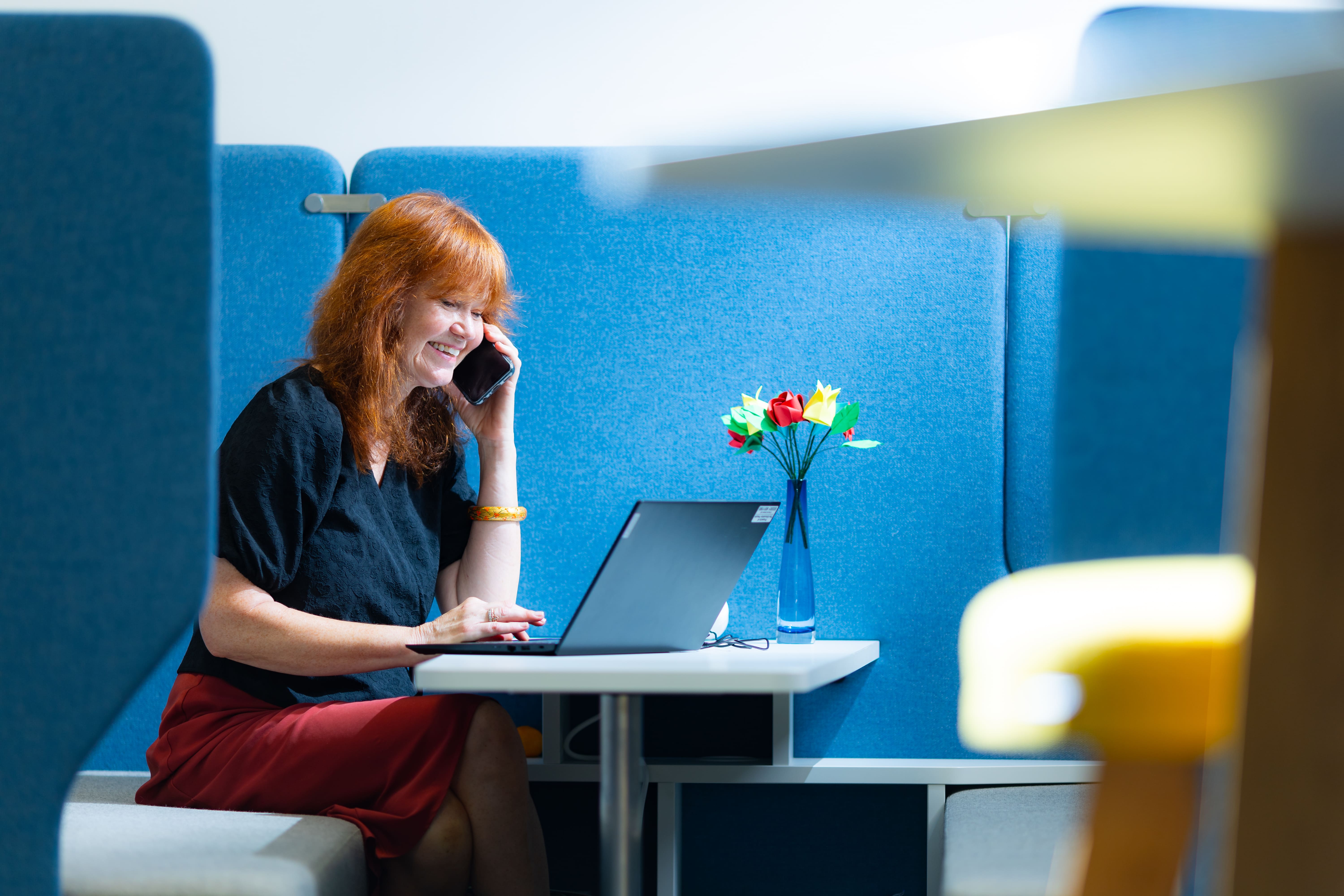 Lady speaking on a mobile phone and using a laptop sitting at a desk